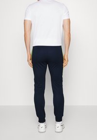 Marinträningsbyxor med gröna sidostråk, elastiska muddar och en slät textur, kombinerade med en vanlig vit t-shirt med kort ärm.