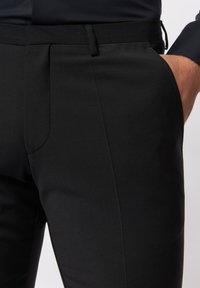 Schwarze, maßgeschneiderte Hosen aus strukturiertem Stoff, mit flacher Vorderseite, Seitentaschen und slim fit Design.