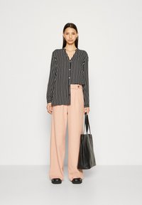 Black and white striped button-up shirt, light pink wide-leg trousers with side button detail, and a textured black tote bag.