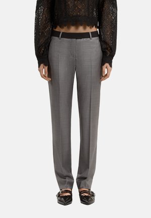 Pantalones rectos grises de tela texturizada, con una cinturilla negra y rayas verticales, combinados con una blusa de encaje negra.