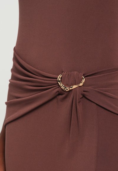 Καφέ ύφασμα φορεμα με στριφτό λεπτομέρεια στη μέση, διαθέτει αξεσουάρ σε χρυσή απόχρωση με λεοπάρ μοτίβο. Απαλή υφή.