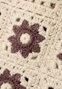 Tessuto all'uncinetto con filato di colore crema, decorato con motivi floreali color bordeaux e pattern a giorno. Tessurizzato, con ricami dettagliati e forme.