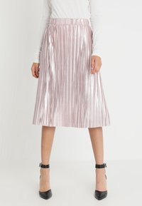 Rosa plissierter Midirock mit glänzendem Finish, elastischer Taille und strukturierter Form, kombiniert mit schwarzen High-Heel-Schuhen.