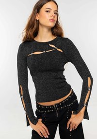 Top negro de manga larga con detalles recortados y acentos metálicos. La tela tiene un ligero brillo. Combinado con pantalones negros de cintura alta con tachuelas.