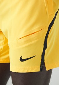 Gula träningsshorts i lättviktig tyg, med en svart Nike-logotyp, sidofickor och kontrasterande svarta sidostråk.