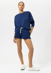 Marineblauw sweatsuit met sweatshirt en shorts, voorzien van een comfortabele pasvorm, ronde halslijn en een taille met trekkoord. Gestructureerde stof met witte accenten.