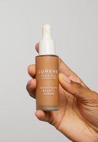 Lumene Instant Glow Beauty Serum i en brun glassdråperflaske med en hvit pipettekork. Teksten på etiketten inkluderer "Usynlig Belysning."