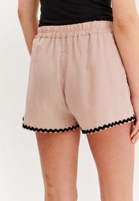Svetloružové šortky s elastickým pásom a čiernym vlnitým lemom na okraji. Vyrobené z ľahkého materiálu s uvoľneným strihom.