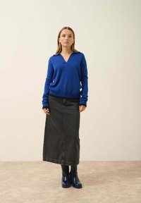 Sininen villa-pulloversi, jossa on V-pääntie ja ribbireunat, yhdistettynä pitkään mustaan denim-hameeseen ja kiiltäviin sinisiin nilkkasaappaisiin. Yksinkertainen, siisti muotoilu.