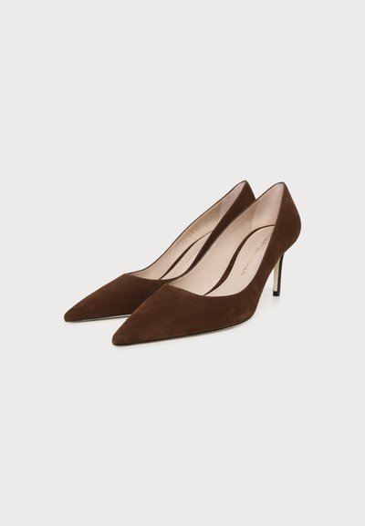 Paire d'escarpins en daim marron à bout pointu avec talons aiguilles sur un fond clair.
