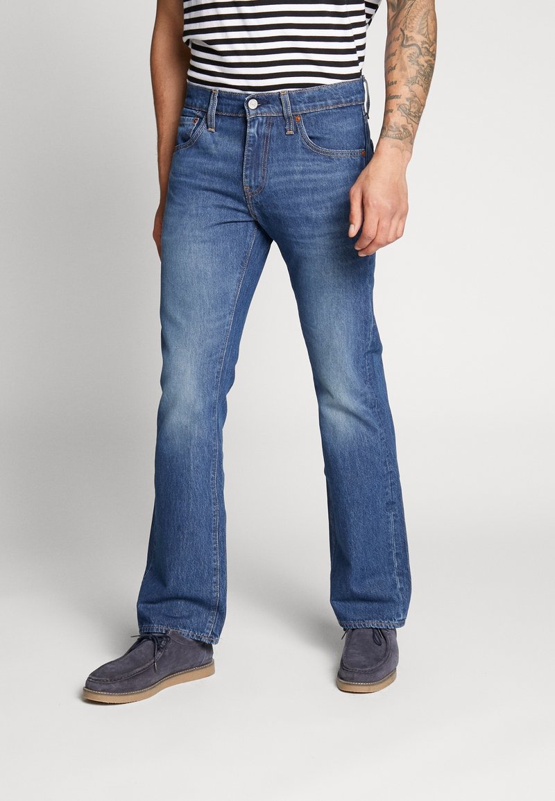 Blå denim jeans med utsvängda ben och ljus tvätt, med framfickor och knäppning. Stylat med en randig skjorta och mockaskor.