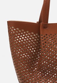 Brun læder tote bag med et perforeret design, der har firkantede udskæringer. Tasken har to solide håndtag og en struktureret overflade.