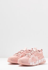 Baskets de sport roses en matériaux suédé et en maille, dotées d'un système de laçage, de semelles épaisses et d'un logo "Hello Kitty" en blanc sur le côté.