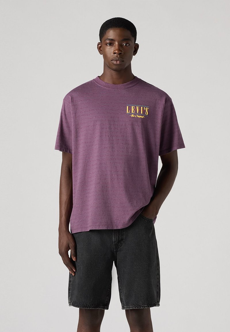 Paarse T-shirt met korte mouwen met een gestructureerd patroon en een gele "LEVI'S The Original" logo. Gemaakt in combinatie met zwarte denimshorts.
