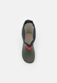 Vihreä vedenpitävä saapas, jossa on teksturoitu päällinen, pyöreä kärki ja meripeninkulman vetotanko punaisella korostuksella kauluksessa. Tasapohjainen muotoilu.