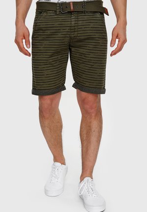Olivenfarvede shorts med sorte vandrette striber, opkrøllede kanter og et brunt bælte. Fuldført med hvide sneakers.
