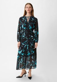 Schwarzes durchsichtiges Kleid mit blauem abstraktem Blumenmuster, langen Ärmeln, Schlüsselloch-Ausschnitt und tailliertem Bund, kombiniert mit schwarzen spitzen Absätzen.