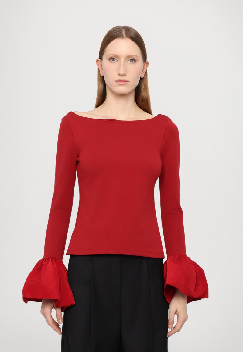 Red top with a boat neckline, fitted bodice, and dramatic long sleeves with gathered cuffs. The fabric appears smooth and textured.