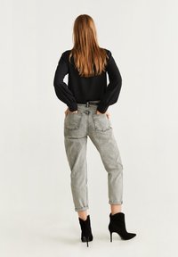 Blusa nera a maniche lunghe, jeans grigi a vita alta con risvolti, e stivaletti neri con tacco alto. Tessuto morbido con una vestibilità comoda.