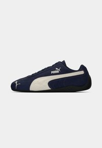 Mørkeblå atletisk sko lavet af ruskind og tekstilmaterialer. Har et hvidt PUMA-logo og accenter, lav profil og tekstureret sort sål.