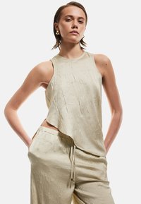 Top senza maniche color beige chiaro con finitura texturizzata e orlo asimmetrico, abbinato a pantaloni texturizzati coordinati con vita elastica.