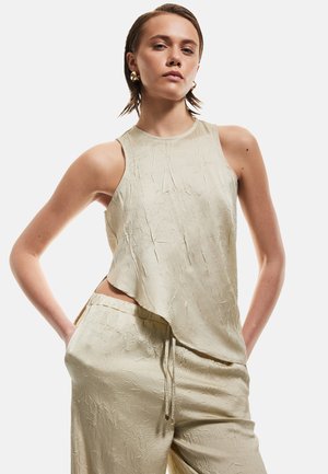 Top senza maniche color beige chiaro con finitura texturizzata e orlo asimmetrico, abbinato a pantaloni texturizzati coordinati con vita elastica.