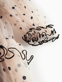 Karmiinroosa tüll, millel on tumesinised täpid, mustade tikanditega voltidega varrukaotsad. Kerge ja poolläbipaistev materjal.