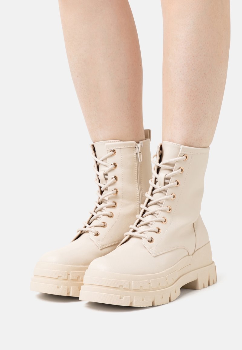 Bottes de combat beiges à lacets, en cuir lisse, avec une semelle épaisse et texturée ainsi que des œillets dorés, dotées d'une fermeture éclair latérale.