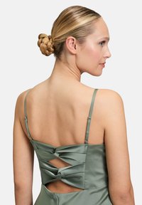 Satin grünes Kleid mit dünnen Trägern, das ein gekreuztes Rückendesign und Ausschnittdetails aufweist, welches eine glatte Textur und einen subtilen Glanz betont.