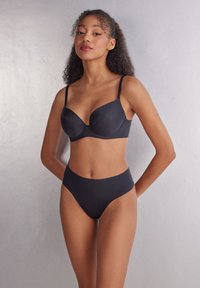 Sostenedor negro sin costuras con un acabado suave y copas contorneadas, combinado con braguitas de cintura alta a juego, ambos con tirantes finos y un diseño minimalista.