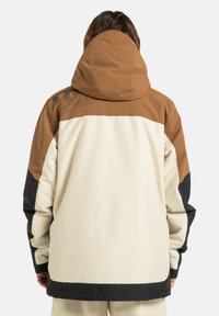 Una giacca con cappuccio dal design a blocchi di colore in marrone, crema e nero, con un pannello texturizzato sulla spalla e una forma rilassata.