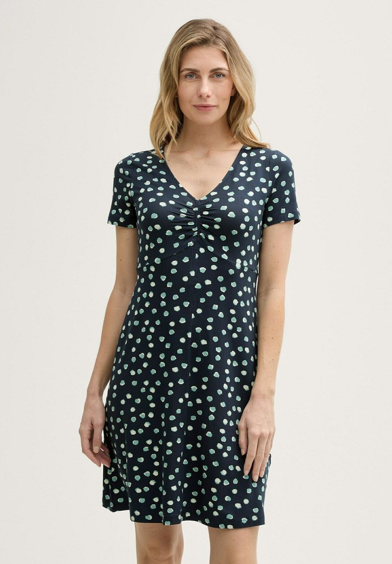 Marineblaues Kurzarmkleid mit V-Ausschnitt, das eine geraffte Vorderseite und ein Muster aus minzgrünen Punkten aufweist. Hergestellt aus leichtem, glattem Stoff.