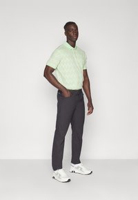 Polo shirt vert clair avec un motif texturé, associé à un pantalon gris foncé et des baskets blanches avec des accents noirs.