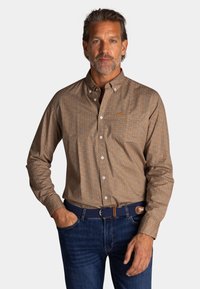Bruine gestreepte langarmshirt met een button-down kraag, voorzien van kleine blauwe en oranje motieven en een borstzak. G gedragen met blauwe jeans.