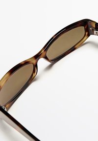 Occhiali da sole tartarugati con lenti marroni, design della montatura curvo e finitura lucida. Accenti in metallo argentato sulle astine.