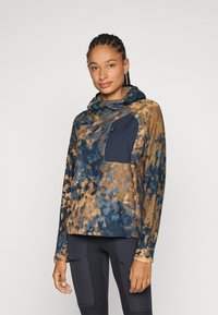 Fleece pullover in een bruine en blauwe tie-dye patroon, met een marineblauwe zak, capuchon en lange mouwen. Zachte textuur met een afgeronde onderrand.