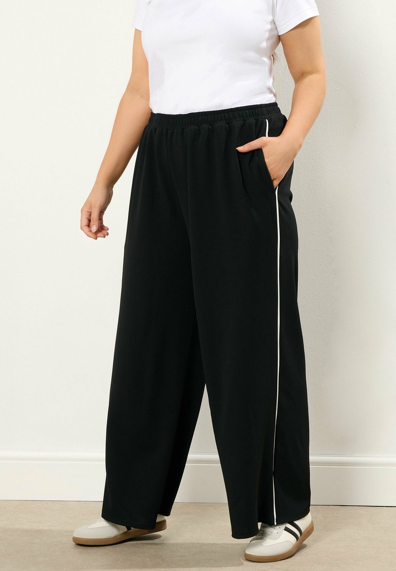 Svarta vida byxor med elastisk midja, med vita sidostreck och sidofickor; kombineras med en vit T-shirt och lätta skor.