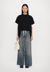 T-shirt nera oversize, jeans in denim azzurro chiaro a gamba larga con cordoncino, borsa bianca e scarpe nere. Texture liscia, design casual.