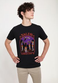 Černé bavlněné tričko s barevným grafickým motivem šesti postav v šortkách a sportovním oblečení, s nápisem "SALEM SUMMER CAMP '78."
