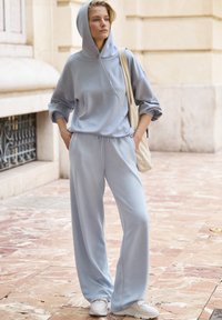 Sudadera con capucha azul claro de mangas sueltas, combinada con pantalones de chándal de pierna ancha a juego. Zapatillas blancas completan el atuendo.