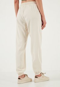 Crème kleurige joggers met elastische boorden en tailleband, met een gladde textuur. Gepaard met beige sneakers met metalen accenten.