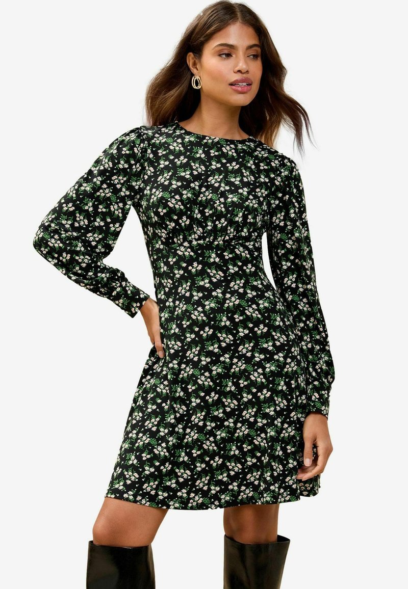 Vestido negro de flores con mangas largas abullonadas y cintura ajustada, que presenta patrones florales en blanco y verde. Combinado con botas altas negras.