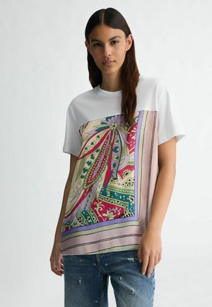 White t-shirt featuring a large, colorful printed design with floral and geometric patterns. Short sleeves, relaxed fit, and smooth fabric texture.