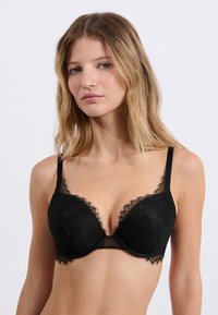 Soutien-gorge en dentelle noire avec un bonnet lisse et rembourré, motifs floraux, bordure en dentelle transparente, bretelles réglables et support à armature.