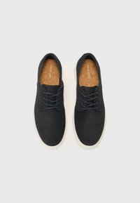Zapatos negros hechos de un material suave con una suela ligera, que cuentan con un diseño clásico de cordones y una plantilla de corcho.