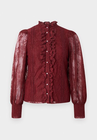 Burgundia pitspluus kõrge rööriga kraega, ees nööbitav, pikkade läbipaistvate varrukatega ja soonikkoega mansettidega. Omab keerukaid pitsimustreid ja detaile.