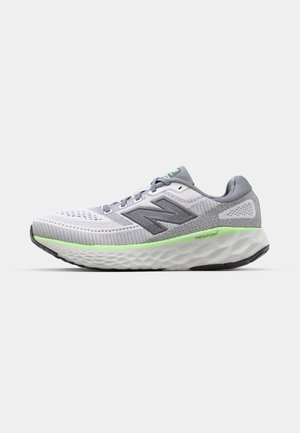 Scarpa atletica bianca e grigia con una tomaia in rete, dettagli testurizzati, un accento verde sulla suola intermedia e un design della suola imbottita.