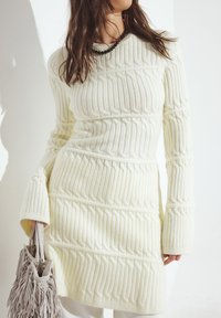 Balta ribota adīta kleita ar garām piedurknēm, ar vertikālām līnijām un brīvu piegriezumu. Pabeigta ar frēzi pelēku rokassomiņu.