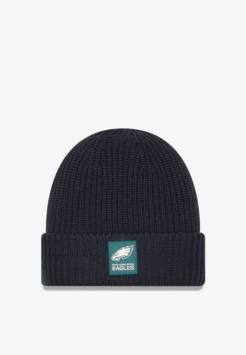 Bonnet tricoté bleu marine foncé avec un revers. Il présente un patch logo vert et blanc des Philadelphia Eagles à l'avant. Tissu texturé.