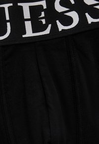 Μαύρο ύφασμα με ορατή ραφή κάτω από μια φαρδιά μαύρη ζώνη μέσης που φέρει μεγάλα λευκά κεφαλαία γράμματα, εμφανίζοντας εν μέρει τη λέξη "UES".